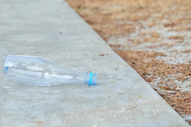 一个塑料瓶的饮用水乱扔在一个道路公园,旁边是一排模糊的垃圾桶
